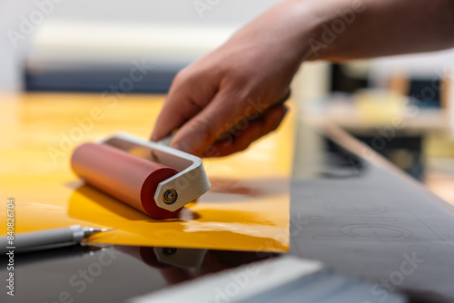The hand of a man who is at work in the production of advertising stickers and holds a roller.