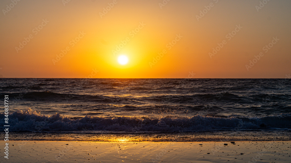 Beautiful sunset over a sandy beach with the sun setting into the sea. Golden light reflects off the calm waves, creating a serene and picturesque coastal scene perfect for relaxation and nature-theme Beautiful sunset over a sandy beach with the sun setting into the sea. Golden light reflects off the calm waves, creating a serene and picturesque coastal scene perfect for relaxation and nature-theme
