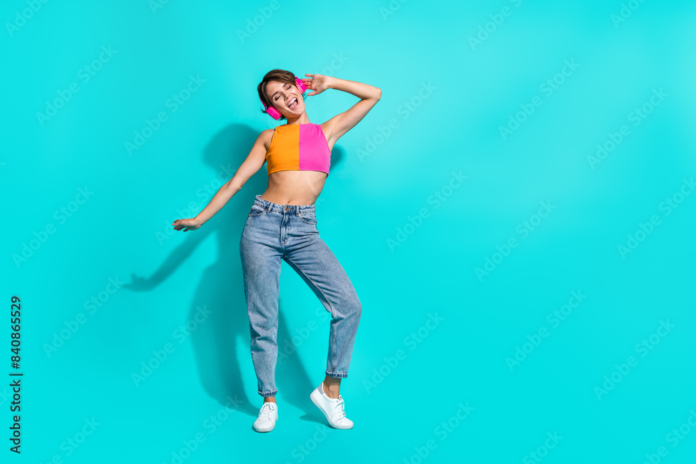 Full length photo of pretty excited woman wear top singing enjoying music headphones empty space isolated teal color background Full length photo of pretty excited woman wear top singing enjoying music headphones empty space isolated teal color background
