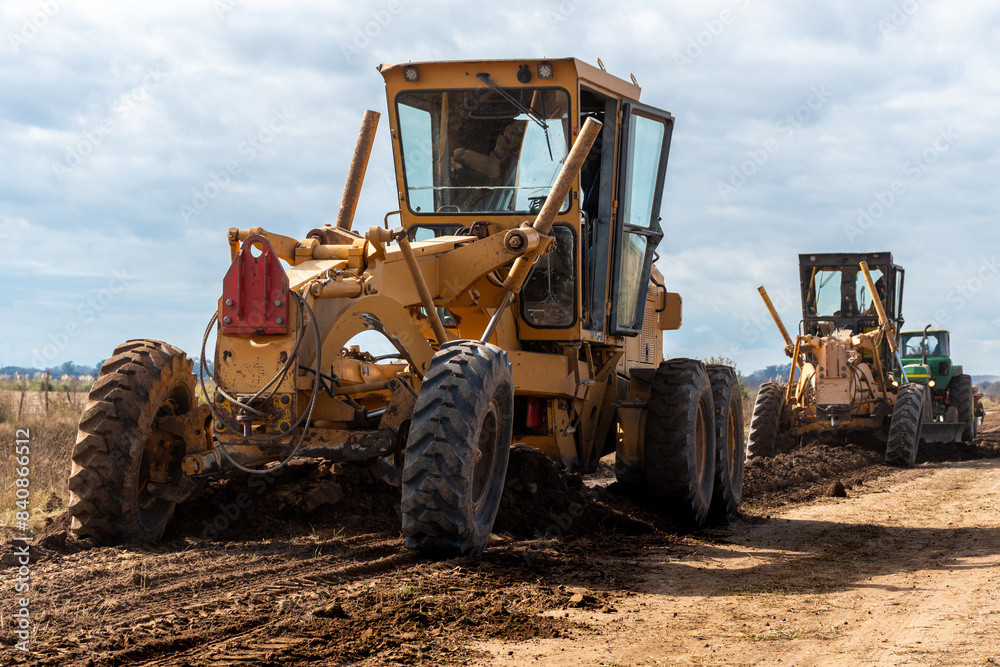 Maquinaria pesada niveladora trabajando en la construcción de una carretera de tierra bajo un cielo despejado Maquinaria pesada niveladora trabajando en la construcción de una carretera de tierra bajo un cielo despejado