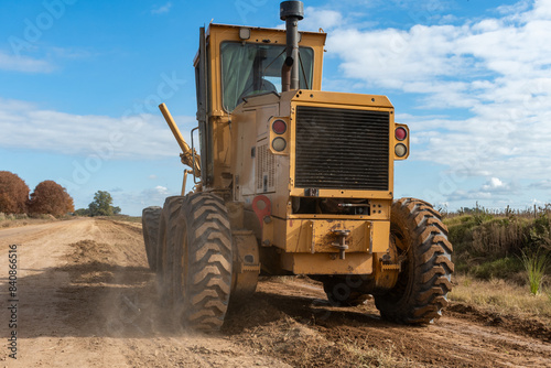 Maquinaria pesada niveladora trabajando en la construcción de una carretera de tierra bajo un cielo despejado