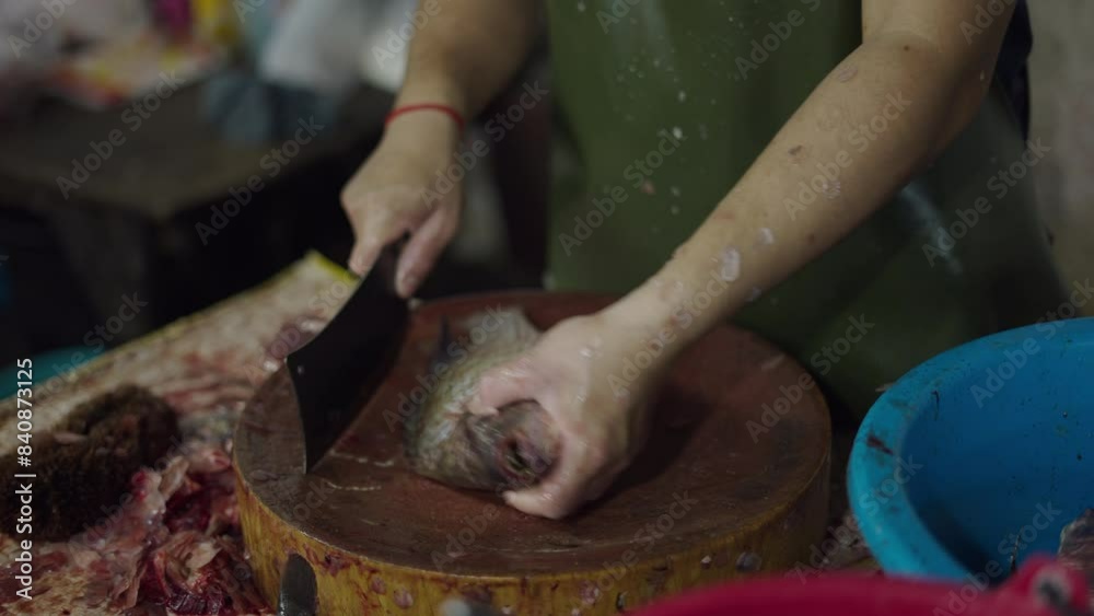 Fisherman cleaning and cutting raw fish on a round wood with a big knife at a local market Fisherman cleaning and cutting raw fish on a round wood with a big knife at a local market