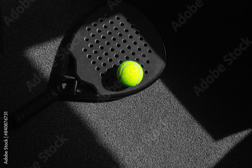 Fotografie Black professional paddle tennis racket and ball with natural lighting on black background
