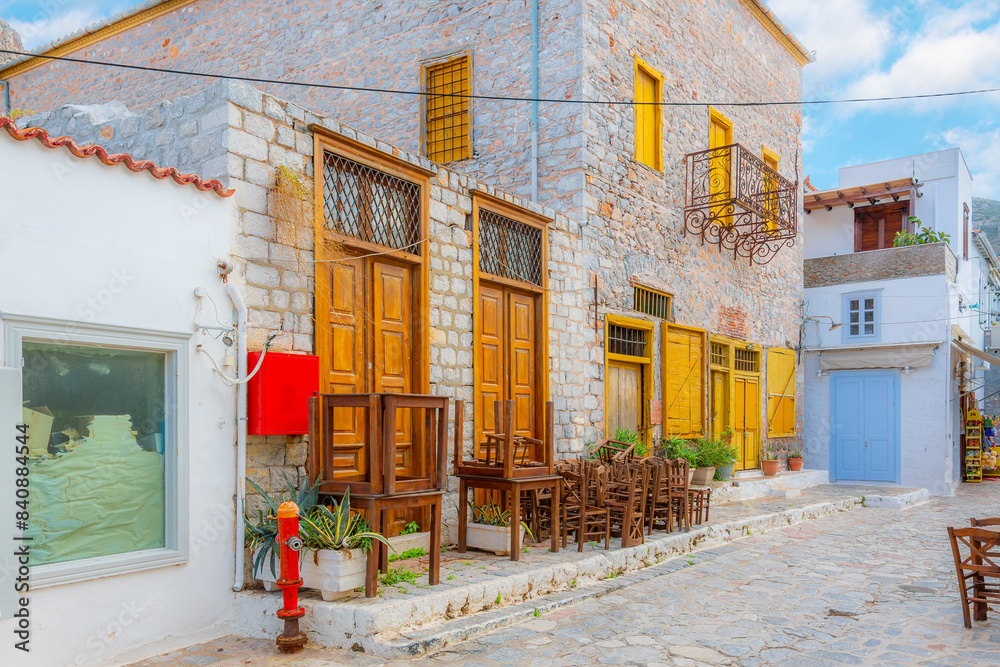 Obraz premium A small sidewalk cafe with chairs stacked before opening hours in the seaside fishing village of Hydra, on the island of Hydra, Greece.