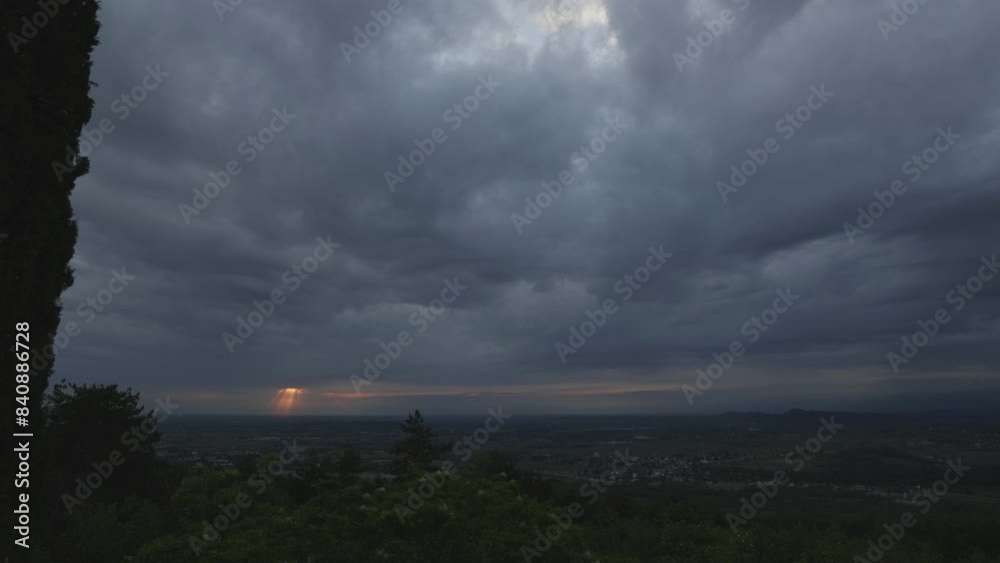 video a intervallo di tempo con vista panoramica, dall'alto su una collina, sul territorio in pianura nel nord est Italia, sotto un cielo scuro e nuvoloso, mentre il sole tramonta dietro le nuvole