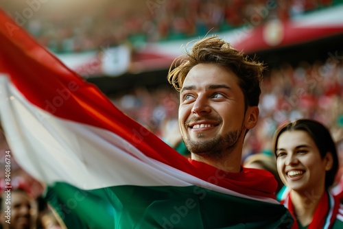 Charismatic young man with a Hungarian flag draped on him, cheering at a public event with pride