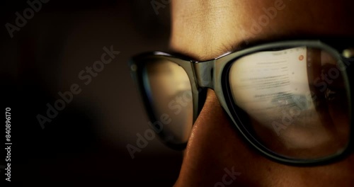 Close-up portrait in profile of part of the face. A young adult Caucasian man wearing glasses whose lenses reflect the reflection of a laptop screen with news on a black background. Fatigue