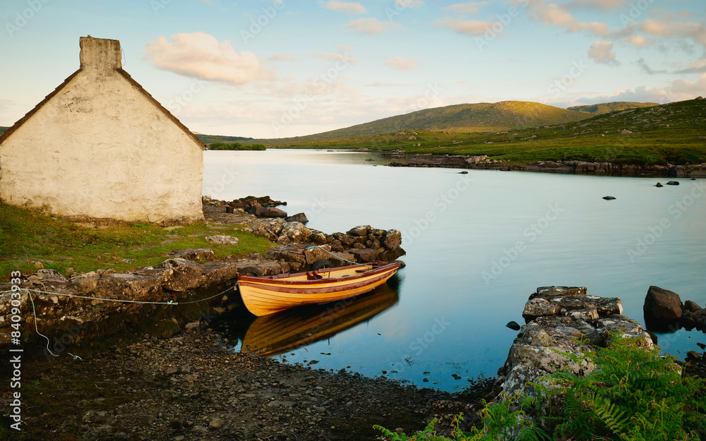 Old wooden fishing boat in lake by Fisherman's hut with mountains in background at Connemara, Galway, Ireland