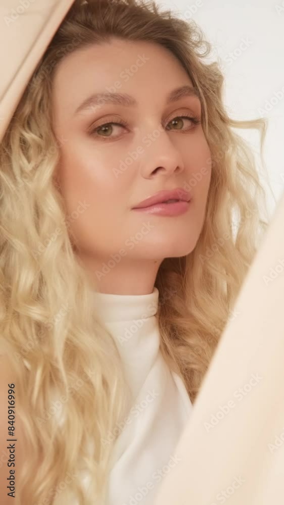 A beautiful woman with curls in a white evening dress posing against a background of beige silk fabric. Beauty face. A beautiful woman with curls in a white evening dress posing against a background of beige silk fabric. Beauty face.