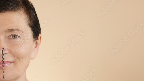 Close-up of happy female face on beige background, free space for advertising cosmetics, beauty care, skin care, spa salons. Half-face of a beautiful Caucasian middle-aged woman 50s age.