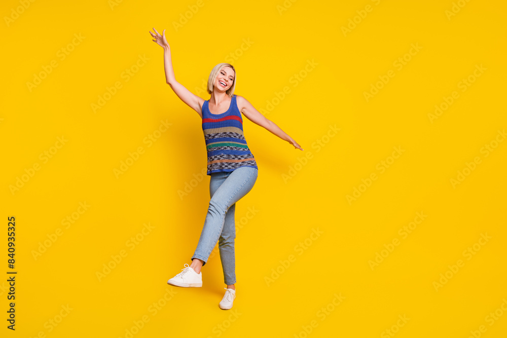 Photo of young positive blonde girlfriend in jeans and singlet dancing at nightclub hands up chilling isolated on yellow color background Photo of young positive blonde girlfriend in jeans and singlet dancing at nightclub hands up chilling isolated on yellow color background