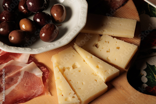 tagliere di legno con una scodella di olive nere, fette di formaggio e prosciutto crudo come antipasto