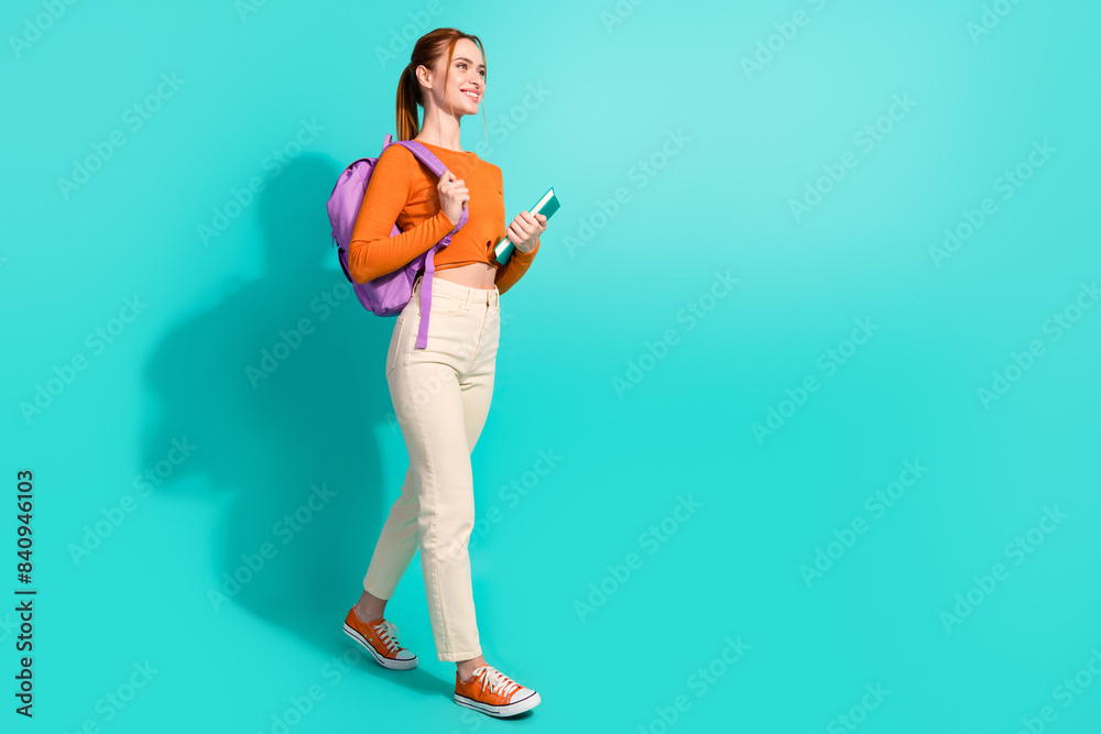 Full length photo of smart woman wear orange crop top pants hold rucksack copybooks go empty space isolated on turquoise color background Full length photo of smart woman wear orange crop top pants hold rucksack copybooks go empty space isolated on turquoise color background