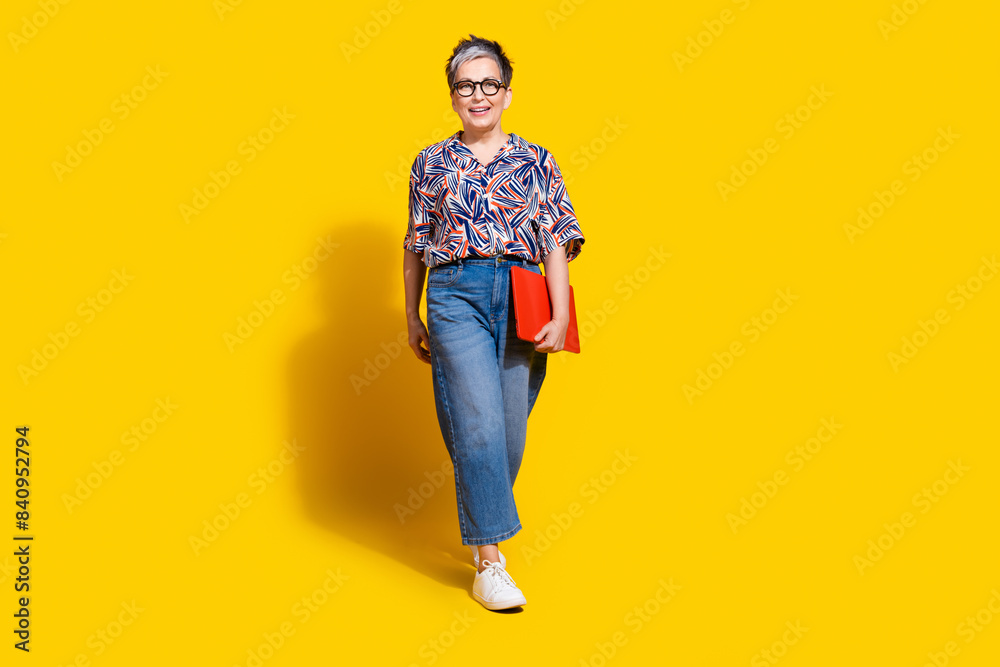 Fototapeta premium Full length photo of lovely senior lady hold netbook walking dressed stylish colorful garment isolated on yellow color background