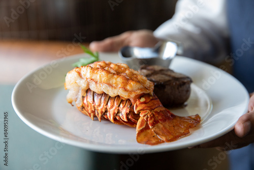 Waiter hold a plate with lobster tail and filet mignon.
