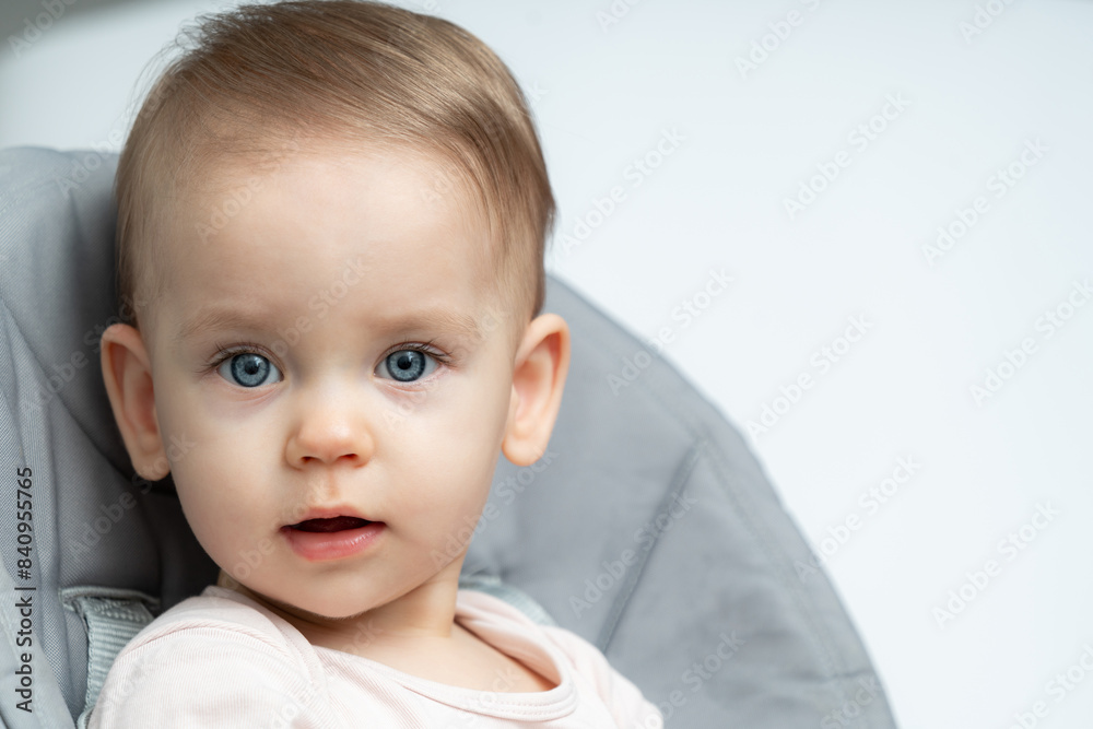 Close-up of a toddler baby gazing at the camera with calm face sitting in high chair Close-up of a toddler baby gazing at the camera with calm face sitting in high chair
