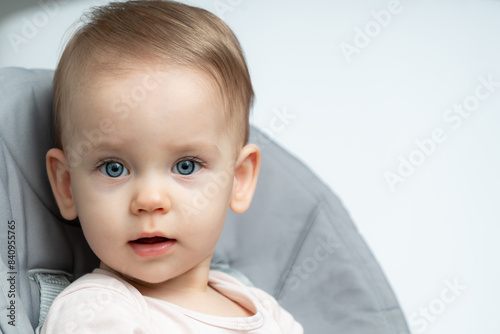 Close-up of a toddler baby gazing at the camera with calm face sitting in high chair