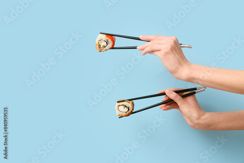 Hands with tasty sushi rolls and chopsticks on blue background