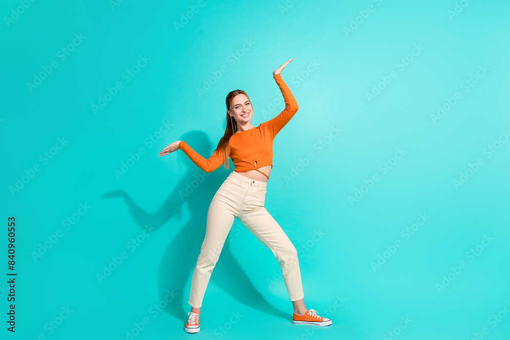 Full size photo of lovely nice girl dressed orange shirt pants arms presenting objects empty space isolated on teal color background Full size photo of lovely nice girl dressed orange shirt pants arms presenting objects empty space isolated on teal color background