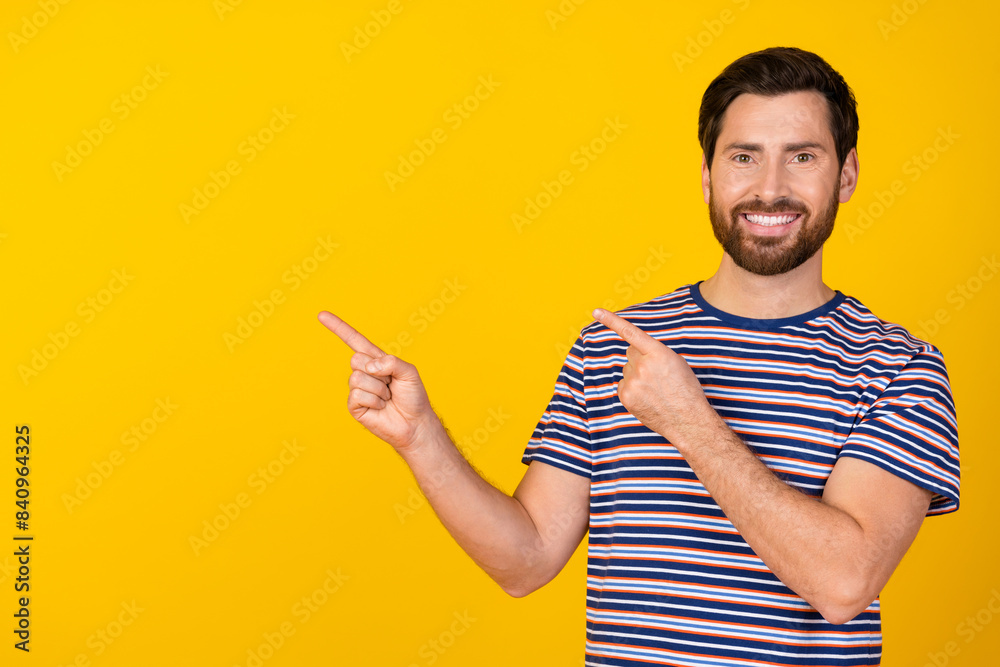Photo of positive man with stylish beard dressed striped t-shirt directing at discount empty space isolated on yellow color background Photo of positive man with stylish beard dressed striped t-shirt directing at discount empty space isolated on yellow color background