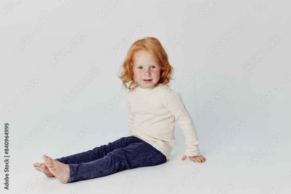 Adorable little girl with red hair sitting in front of white background, childhood beauty and innocence Adorable little girl with red hair sitting in front of white background, childhood beauty and innocence
