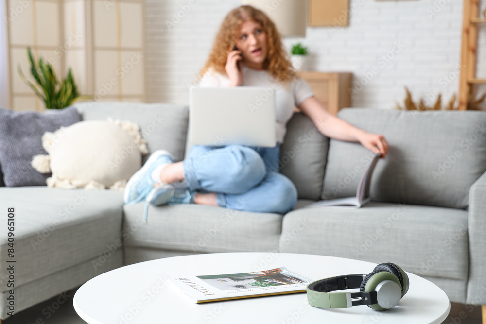 Headphones with magazine on table of woman talking by mobile phone at home, closeup Headphones with magazine on table of woman talking by mobile phone at home, closeup