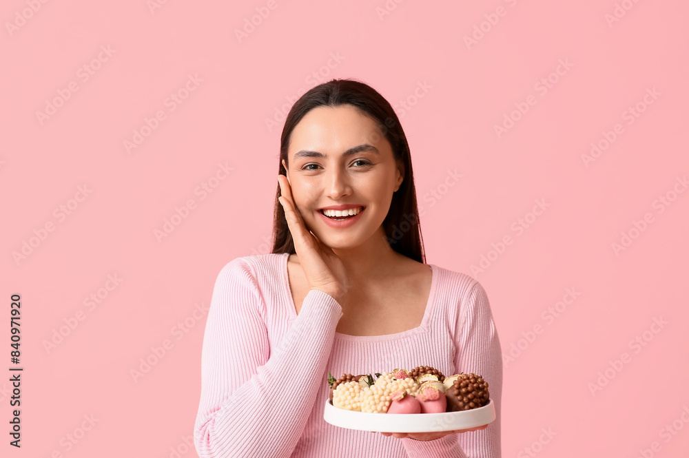 Beautiful young woman holding plate with chocolate covered strawberries on pink background