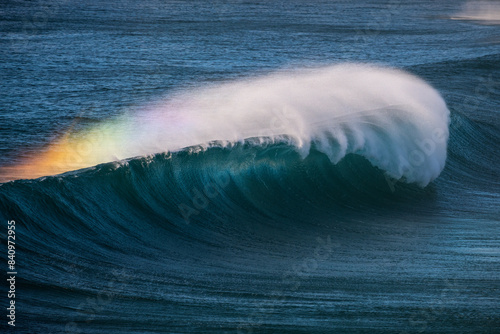 Majestic waves crashing along the coastline of Sydney, Australia, with a vibrant rainbow effect in the mist. 