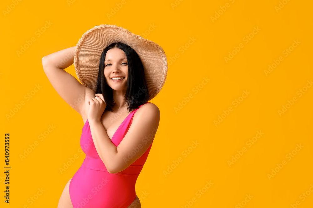 Beautiful young woman in stylish pink swimsuit and wicker hat on yellow background Beautiful young woman in stylish pink swimsuit and wicker hat on yellow background