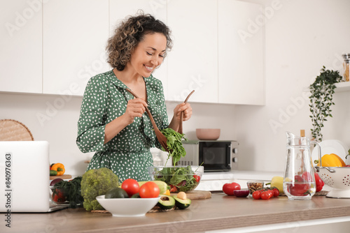 Bild auf Leinwand Mature woman stirring vegetable salad in kitchen