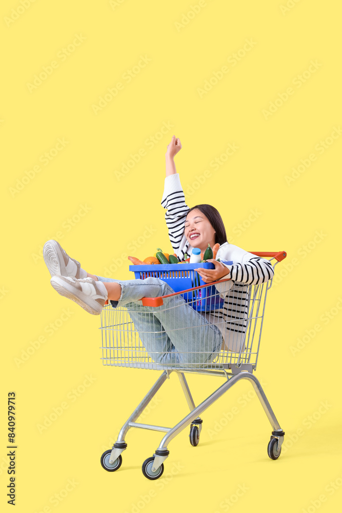 Φωτογραφία Young Asian woman with basket in shopping cart on yellow background