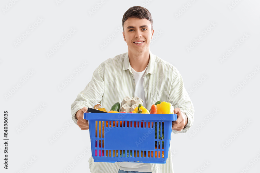 Young man with full shopping basket on light background Young man with full shopping basket on light background