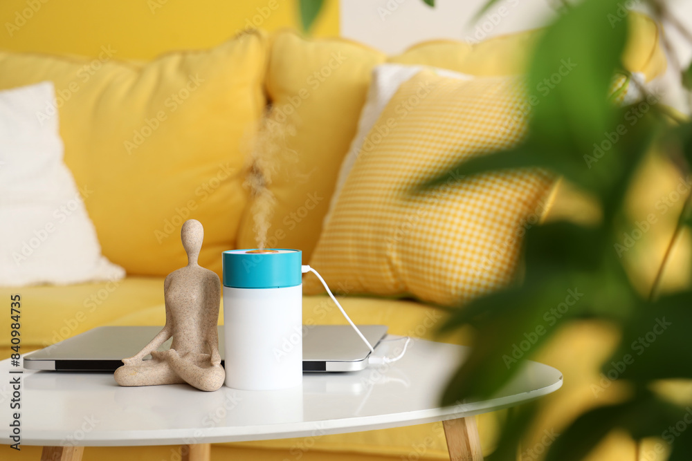 Air humidifier with statuette and laptop on table in living room, closeup Air humidifier with statuette and laptop on table in living room, closeup