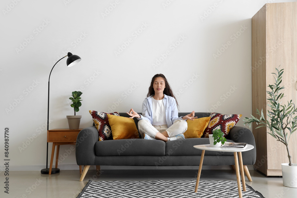 Young Asian woman meditating on black sofa at home Young Asian woman meditating on black sofa at home