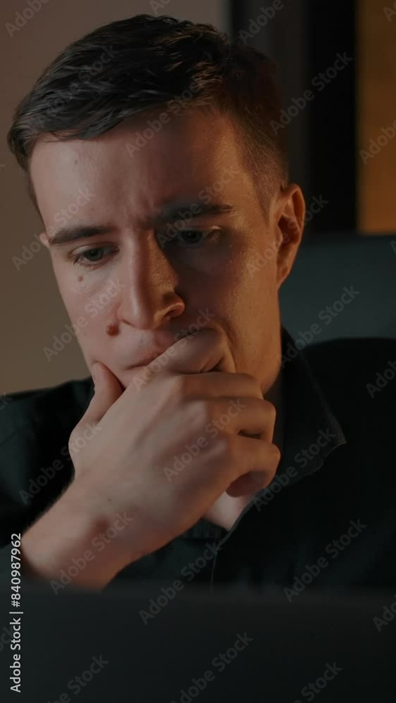 Caucasian male thinking about business solution behind laptop screen. Serious man's face moving closer to notebook screen in evening apartment cozy environment. Vertical shot. Caucasian male thinking about business solution behind laptop screen. Serious man's face moving closer to notebook screen in evening apartment cozy environment. Vertical shot.