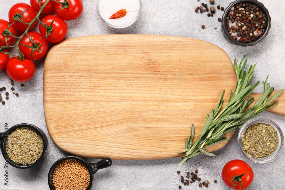 Wooden cutting board surrounded by spices and tomatoes on grey textured table, flat lay. Space for text Wooden cutting board surrounded by spices and tomatoes on grey textured table, flat lay. Space for text