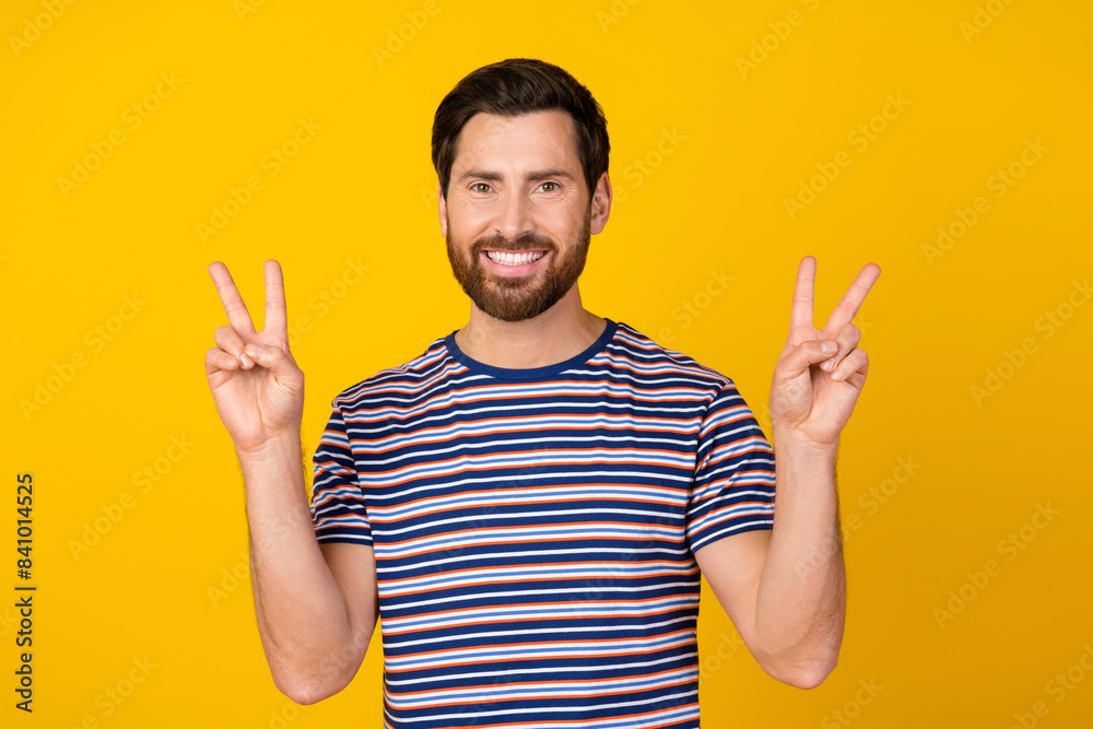 Photo of optimistic handsome man with stylish beard dressed striped t-shirt showing v-sign symbol isolated on yellow color background Photo of optimistic handsome man with stylish beard dressed striped t-shirt showing v-sign symbol isolated on yellow color background
