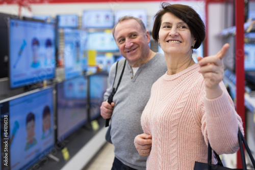 Middle aged man and woman choosing TV while shopping in electronic store. Woman pointing finger.