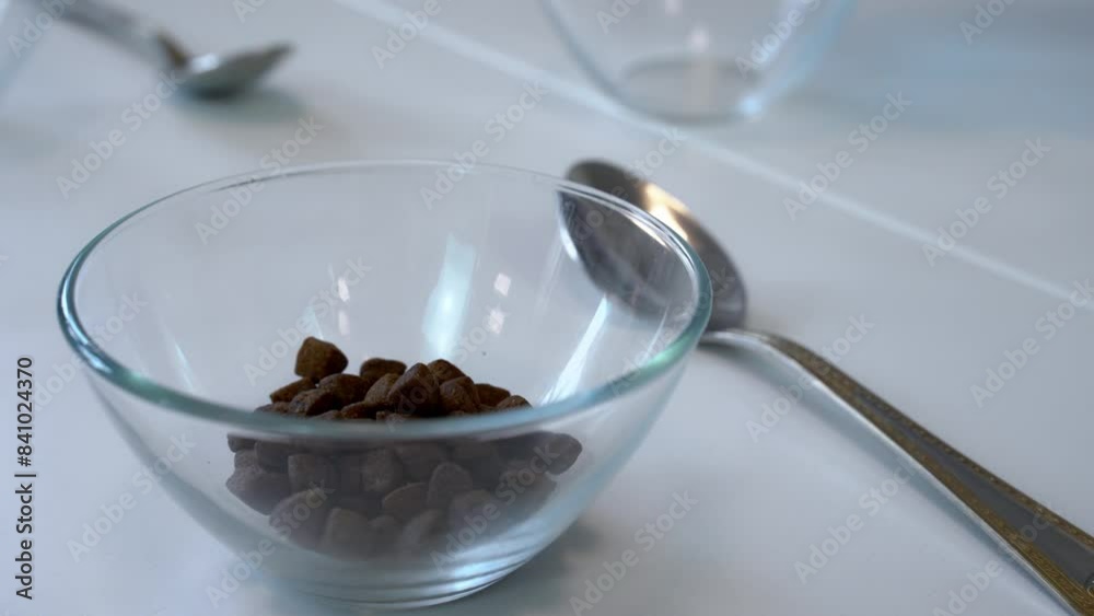 Close-up of hand holding plastic container, pouring dry food, brown dietary supplement granules into transparent cup on set table for two Healthy diet, portion of vitamin calorie control Balanced diet Close-up of hand holding plastic container, pouring dry food, brown dietary supplement granules into transparent cup on set table for two Healthy diet, portion of vitamin calorie control Balanced diet