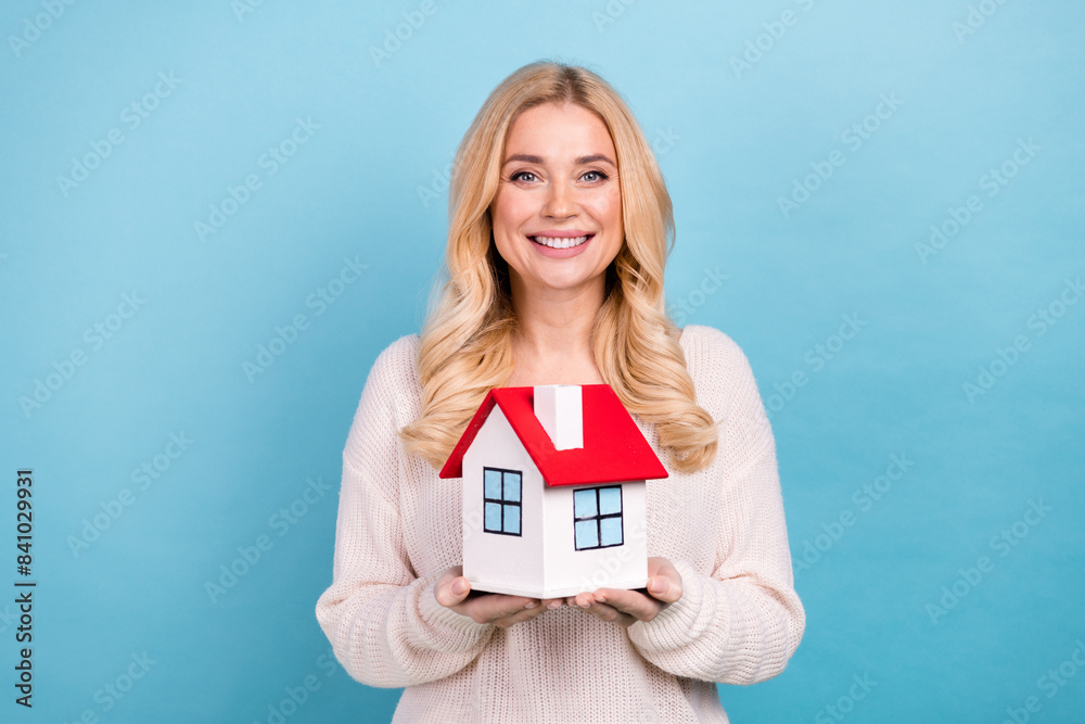 Photo of lovely adorable woman wear stylish white clothes hands hold house isolated on blue color background Photo of lovely adorable woman wear stylish white clothes hands hold house isolated on blue color background