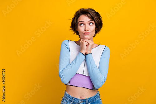Photo of doubtful unsure lady dressed shirt arms chin looking empty space isolated yellow color background photo