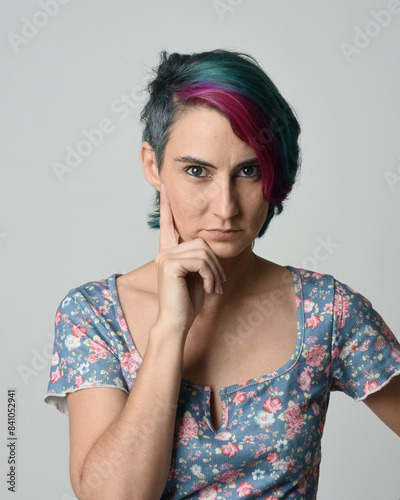 a close up head and shoulders portrait of young alternative female model, with pink and grey shaved undercut hair style, wearing a floral blue top. dramatically pulling expressive facial expressions. 