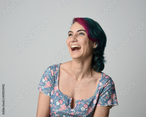 a close up head and shoulders portrait of young alternative female model, with pink and grey shaved undercut hair style, wearing a floral blue top. dramatically pulling expressive facial expressions. 