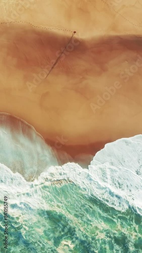Vertical Screen: Aerial view of a person walking on Nazare beach, where sea waves meet the sandy shore, creating a serene scene on Portugals coastline, offering a tranquil and picturesque view photo