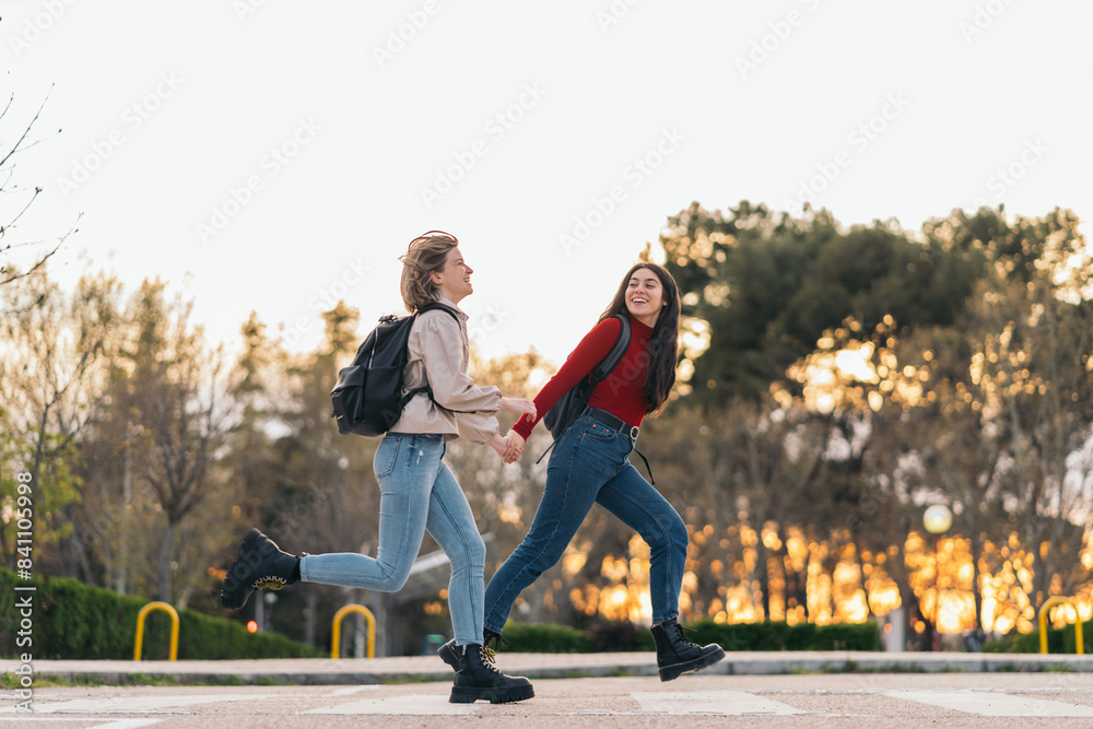 two student girls crossing crosswalk holding her hands, running and smiling two student girls crossing crosswalk holding her hands, running and smiling