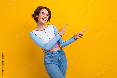 Photo of pretty cheerful lady dressed shirt pointing two fingers empty space isolated yellow color background