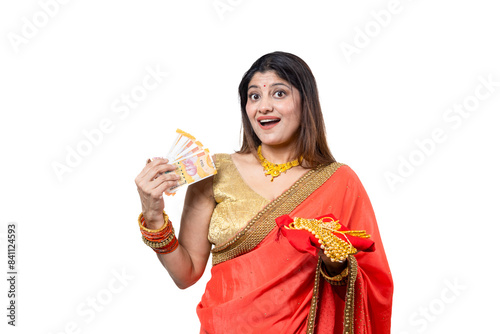 Obraz na plátně Happy young Indian woman wearing red saree holding gold jewelry ornaments in hand and rupee notes standing against white background, Concept of Gold Loan
