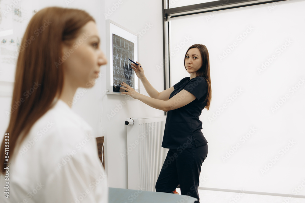 Fototapeta premium medicine, healthcare and people concept - female doctor or vertebrologist showing x-ray image of spine to woman patient at hospital