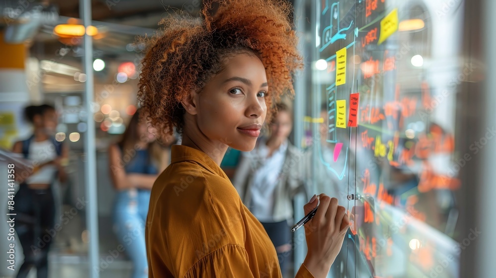 Obraz premium Confident businesswoman using sticky notes on glass wall in office.