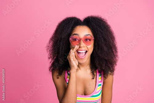 Photo of good mood woman dressed knitwear tank in heart sunglass tell secret sale to empty space isolated on pink color background